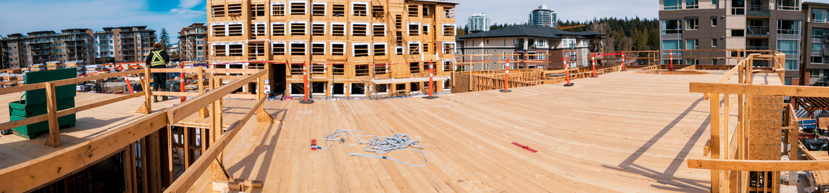 Outdoor daytime upper floor image of hybrid multi family residential Virtuoso building during construction showing cross-laminated timber (CLT) floor panels in place on upper level floor with PPE wearing worker in distance