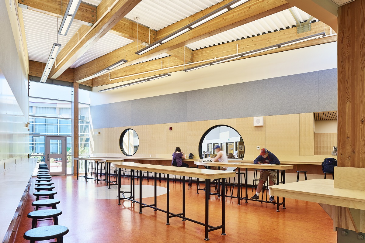 glue-laminated timber (Glulam) beams and columns, decorative wall paneling, corrugated metal ceiling panels are shown in this interior daytime image of the occupied Wellington Secondary School