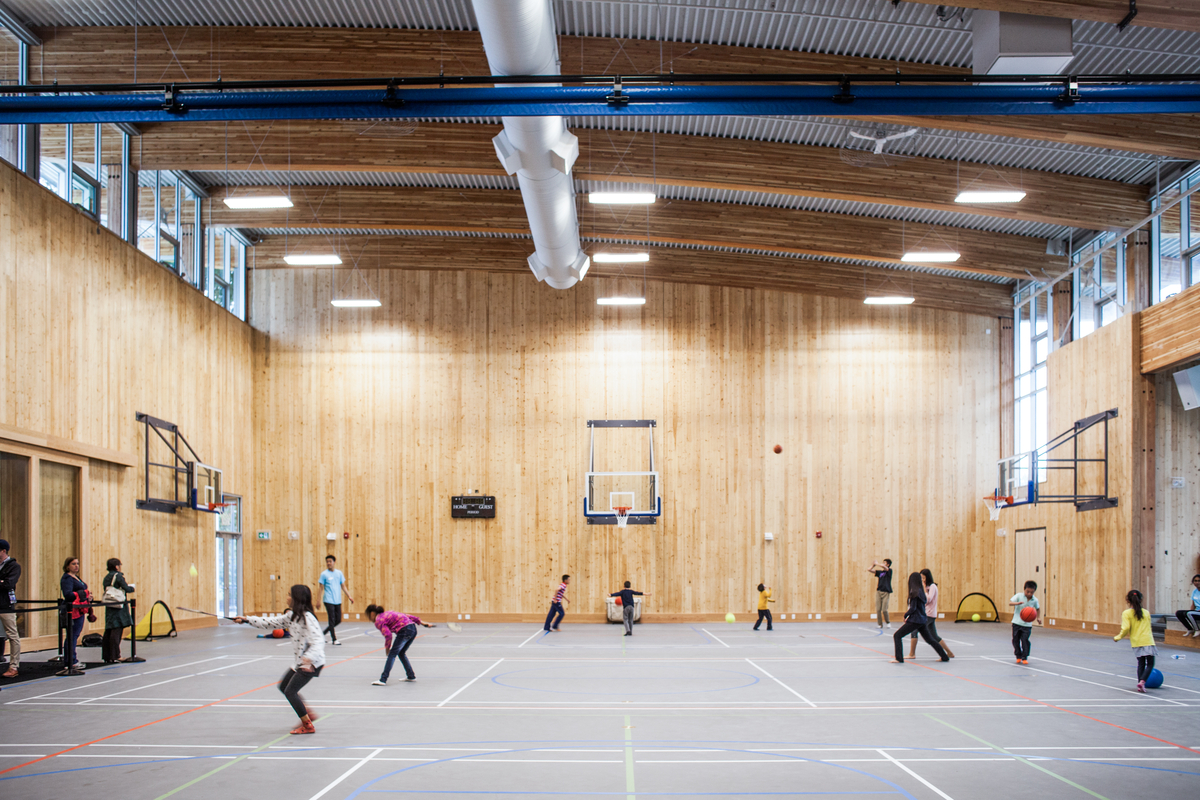 Interior daytime image of occupied Wesbrook Community Centre gymnasium showing cross-laminated timber (CLT) wall paneling and full span arched glue-laminated timber (Glulam) ceiling beams