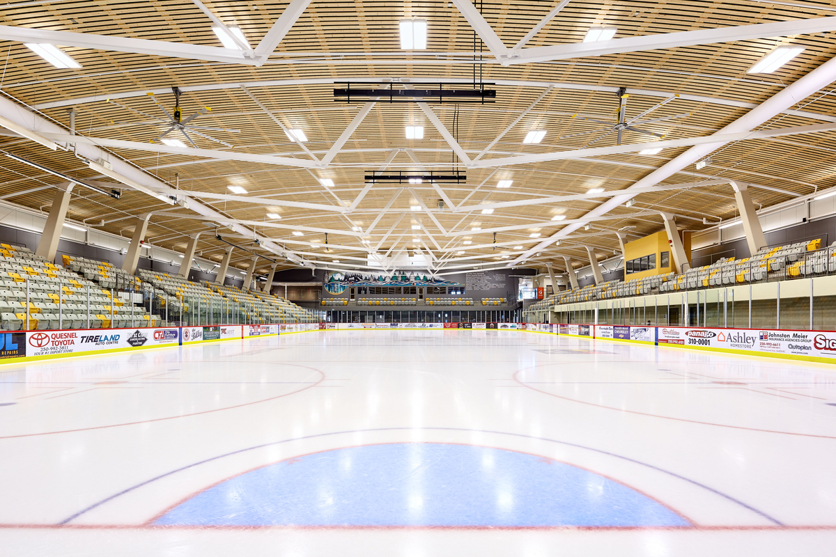 Interior view of low rise West Fraser Centre ice rink showing professional size ice rink, seating for 1,300, arching wood ceiling, and steel supporting trusses.