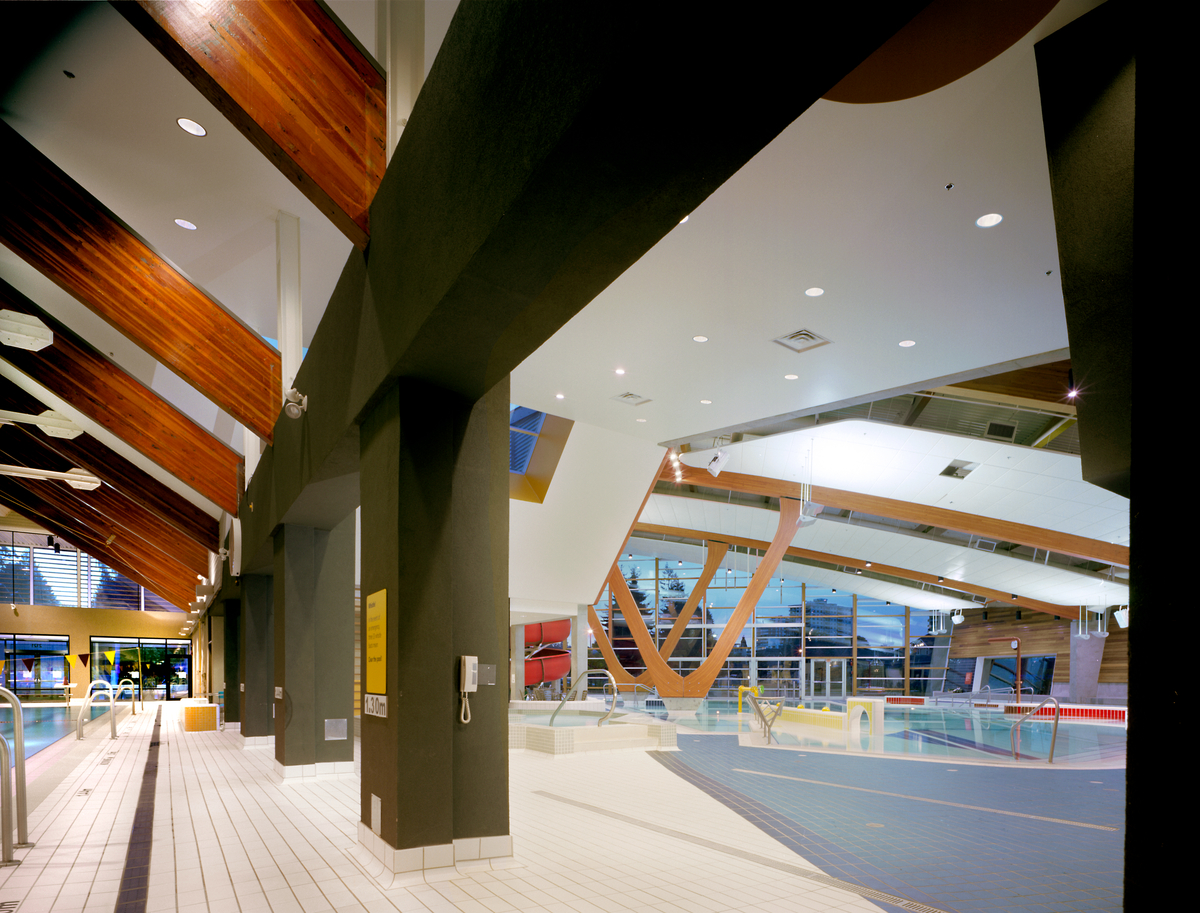 Interior daytime view of low rise West Vancouver Aquatic Centre main pool taken from central pillars between lap pool and family pool and showing arched glue-laminated timber (Glulam) supports