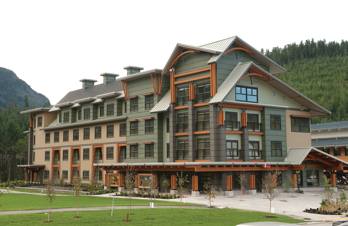 Outdoor cloudy full building image of mid rise Whistler Athlete’s Centre Lodge showing highlighting mass timber usage in exterior beams, columns, trim, and arched roof supports