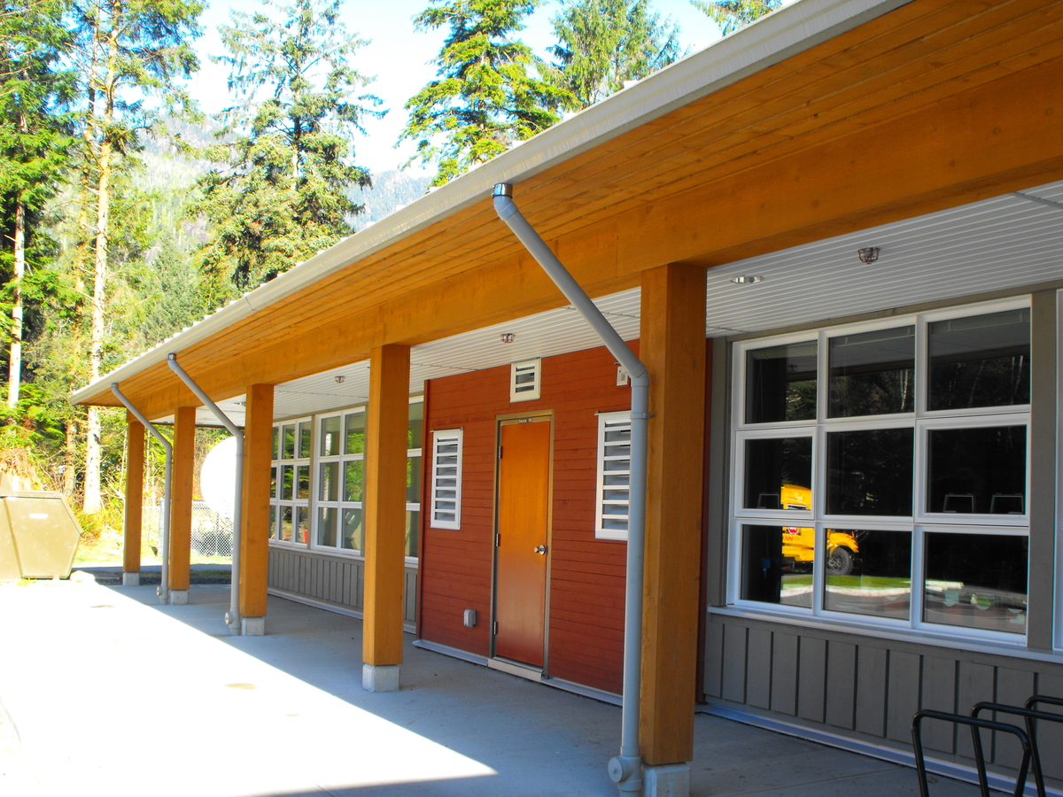 Exterior sunny daytime view of Zeballos Elementary/Secondary School showing wooden soffits and roof supported by Solid-sawn heavy timber columns and beams