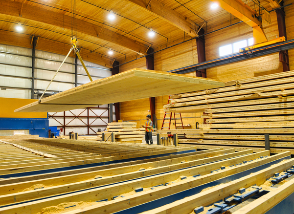 Interior daytime view of worker using bridge crane during CLT panel (cross laminated timber) fabrication process