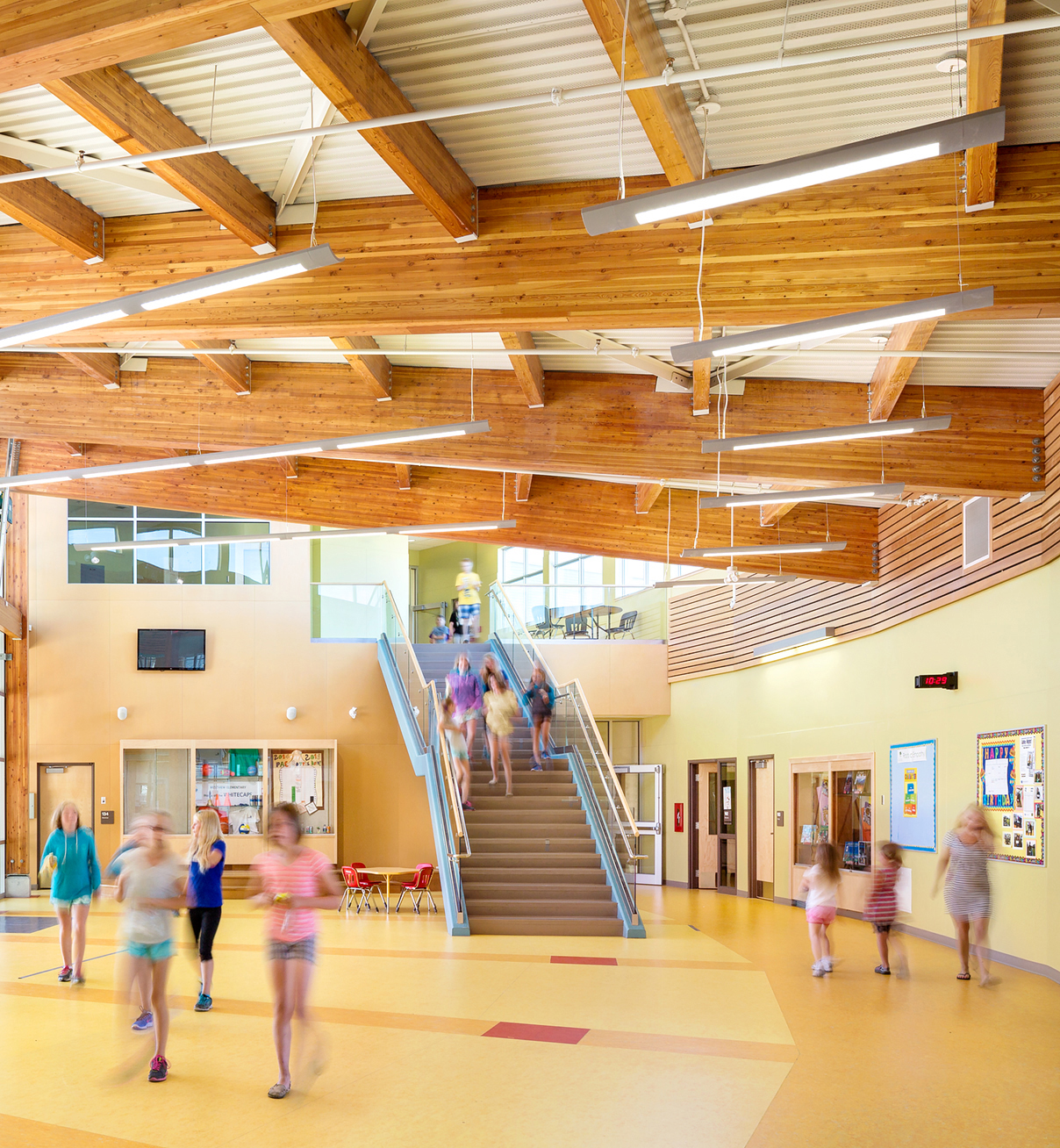 Interior daytime image of low rise Westview Elementary School entrance and two story multi-purpose area complete with students, glue-laminated timber (glulam) beams overhead, and wood accents throughout