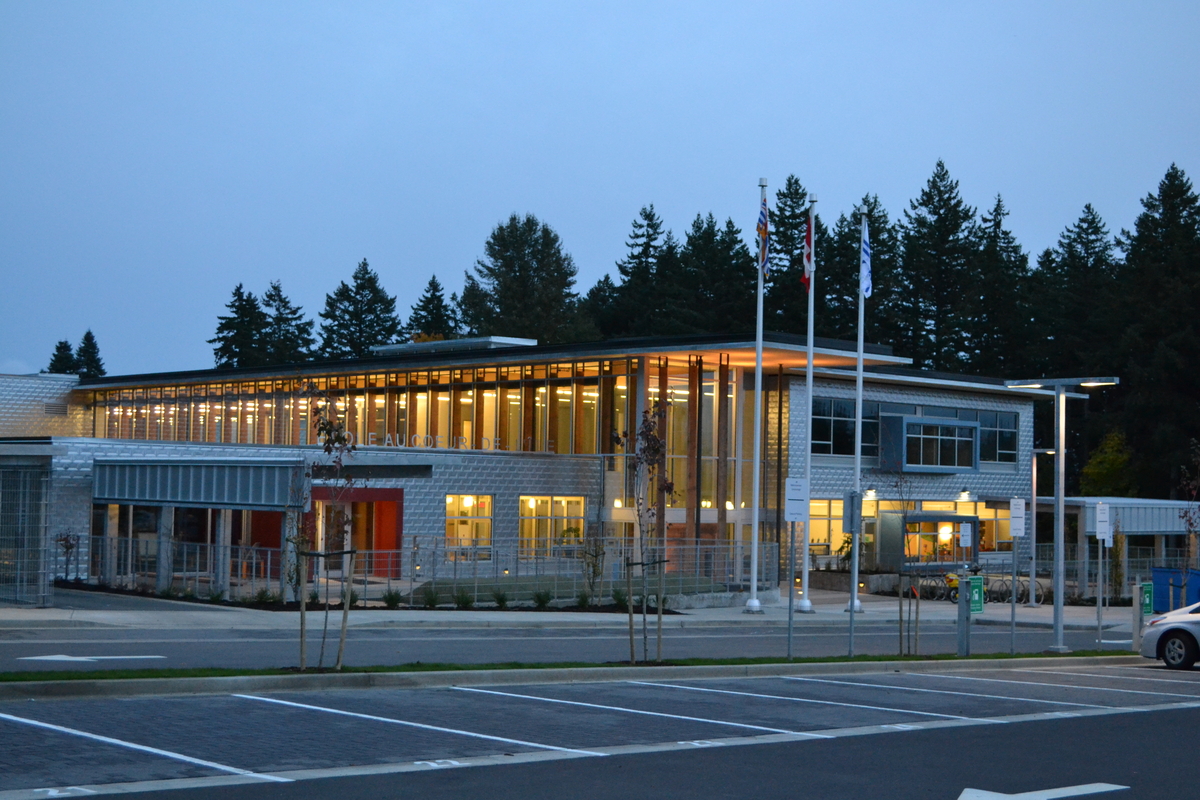 Exterior evening view of low rise hybrid École Au-cœur-de-l’île elementary school building front and two storey main entrance, showing extended roof overhang with cross-laminated timber (CLT) panels supported by solid-sawn heavy timber