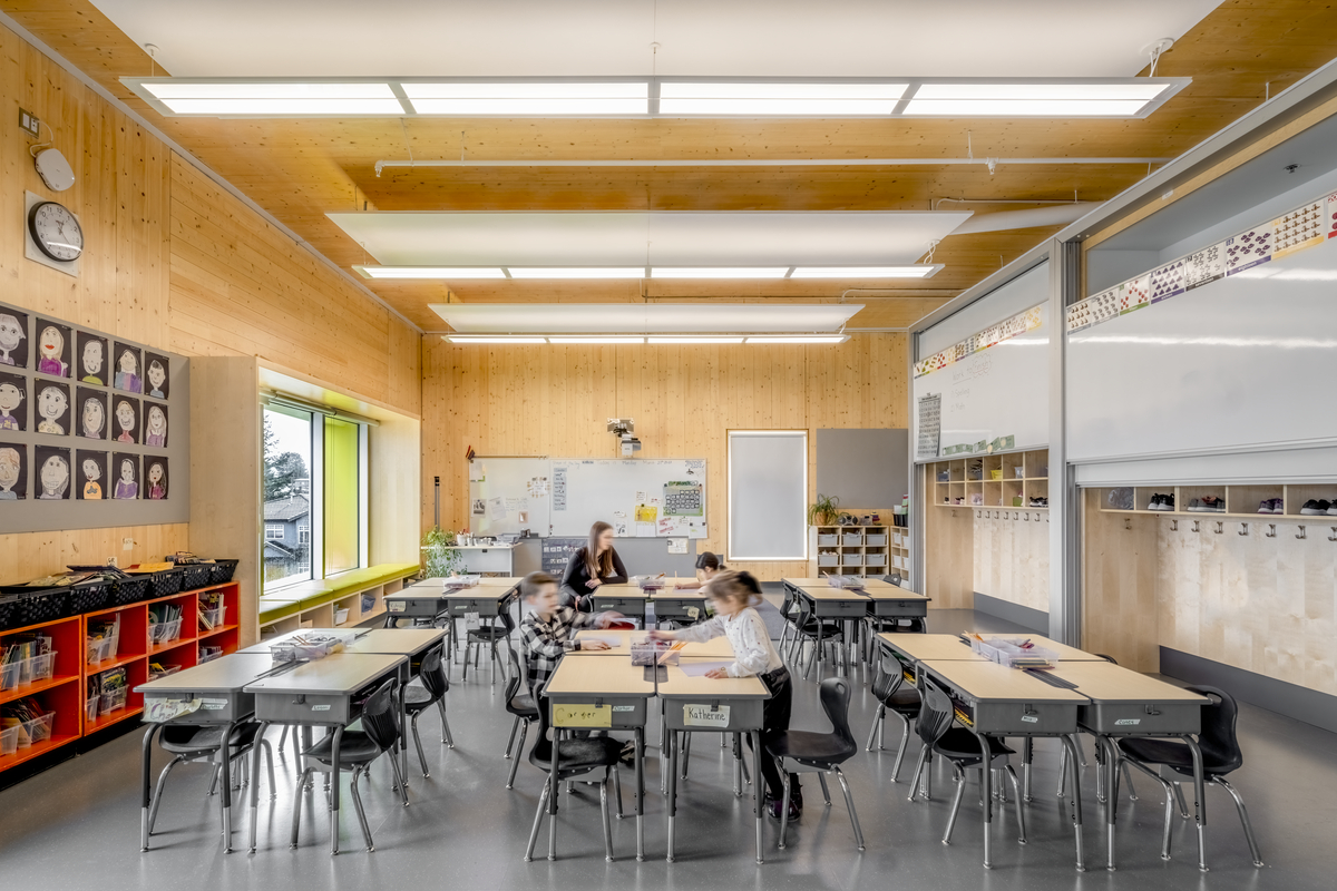 Three students and a teacher working at their desks in a classroom with exposed wood walls and ceiling.