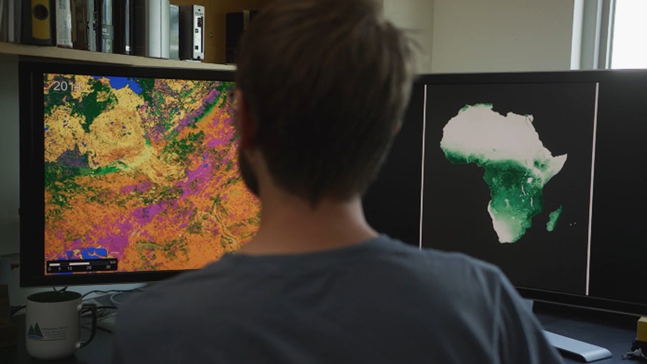 Still image of video, used as icon, showing male looking at dual monitors with resource heatmap on left screen and Africa on right screen