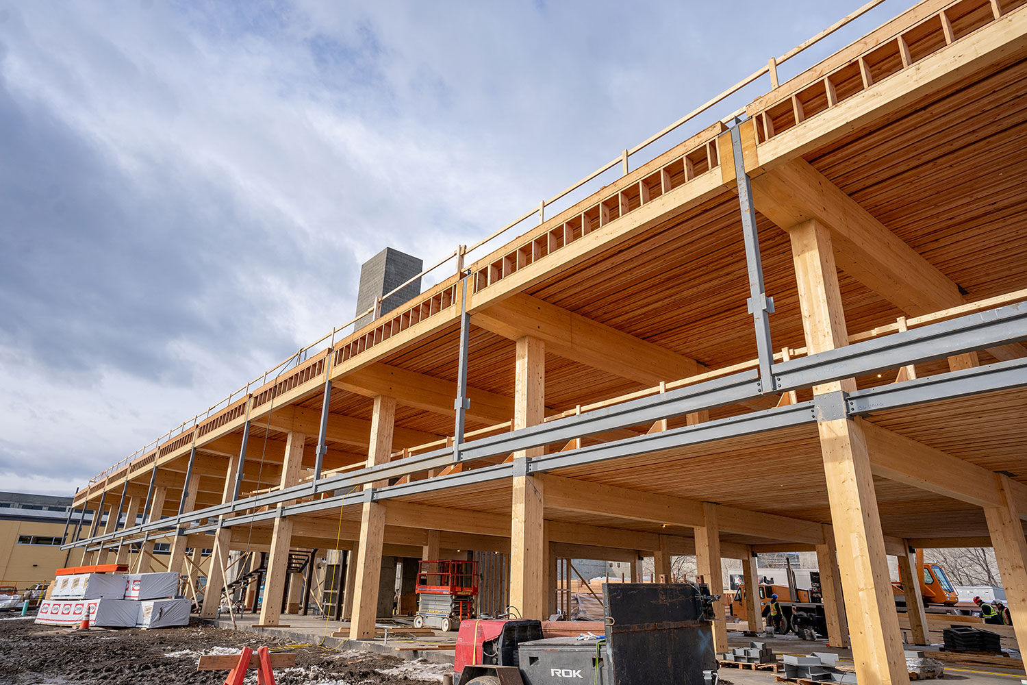 Low-angle photo of the ground floor outside of the partially-built building during the construction of The Exchange. NLT panels for the roof, supported by glulam beams and columns.