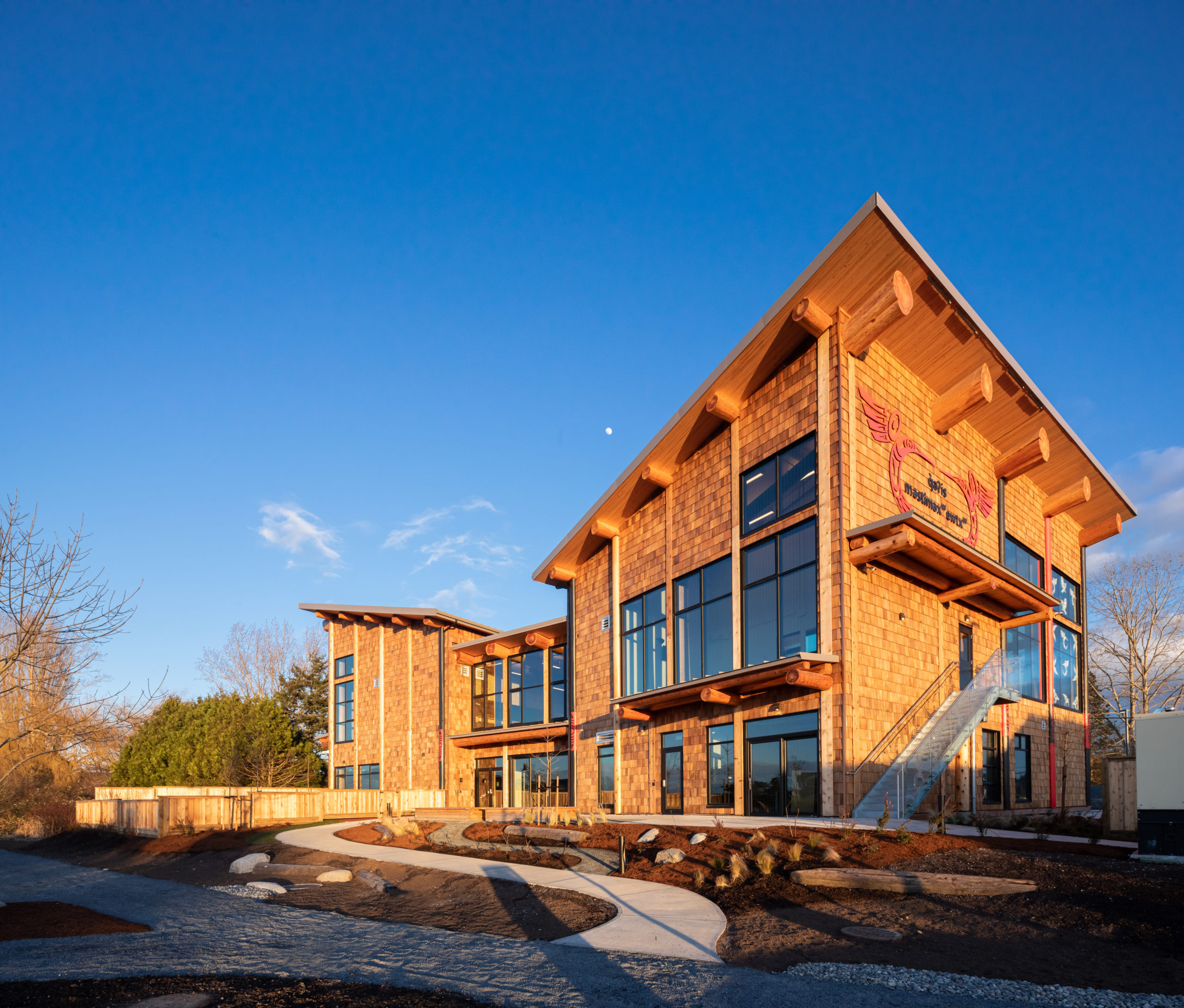 Exterior view of full mass timber building entrance side, with slanted roof and clear sunny sky.