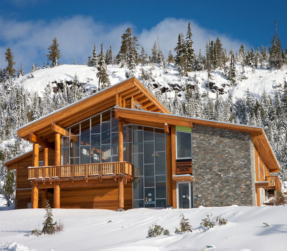 Façade of post-and-beam recreational facility built into the slope of Mount Washington against a backdrop of a snowy mountain and trees.